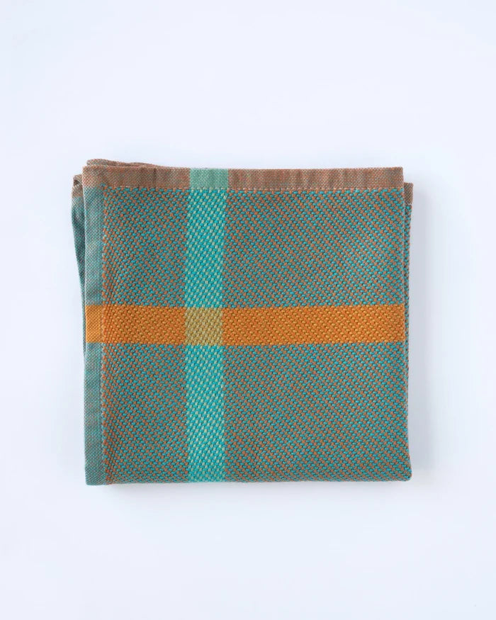 Folded fabric with a plaid pattern featuring green, brown, and orange colors on a white background.