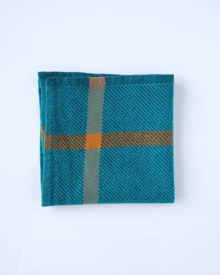 A folded teal woven textile with a plaid pattern in brown and orange, displayed on a clean white background.