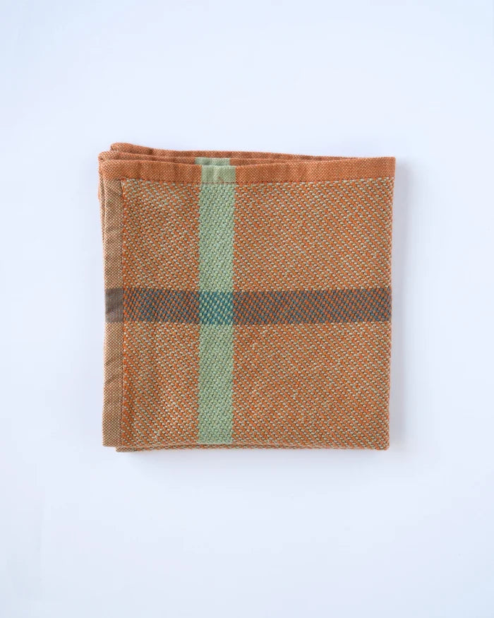 A folded woven textile, likely a pocket square or napkin, featuring a rust-orange base with a vertical sage green stripe and a horizontal dark brown stripe, shown on a plain white background.