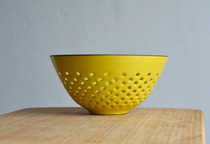 Yellow colander/berry bowl on a wooden surface with a gray background