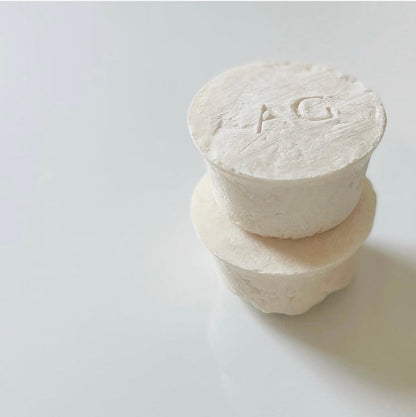 Two stacked white soaps with engraved letters on a light gray background